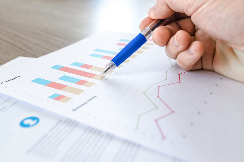 Hand met pen wijst naar grafieken en data analyse rapport met statistieken.