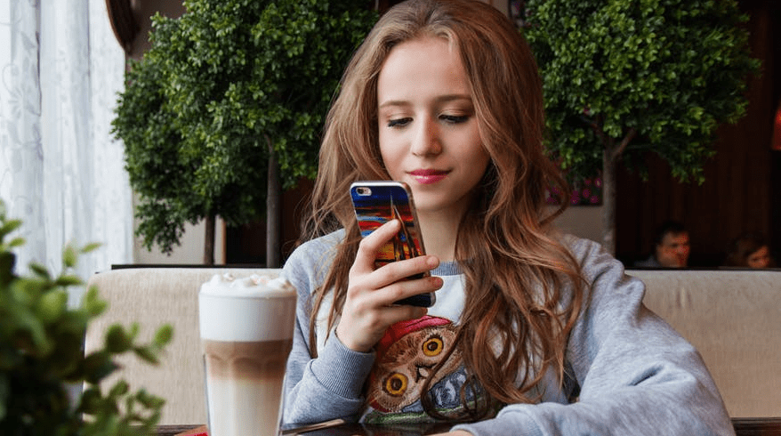 Generatie Z meisje zit op haar telefoon in een café met koffie.