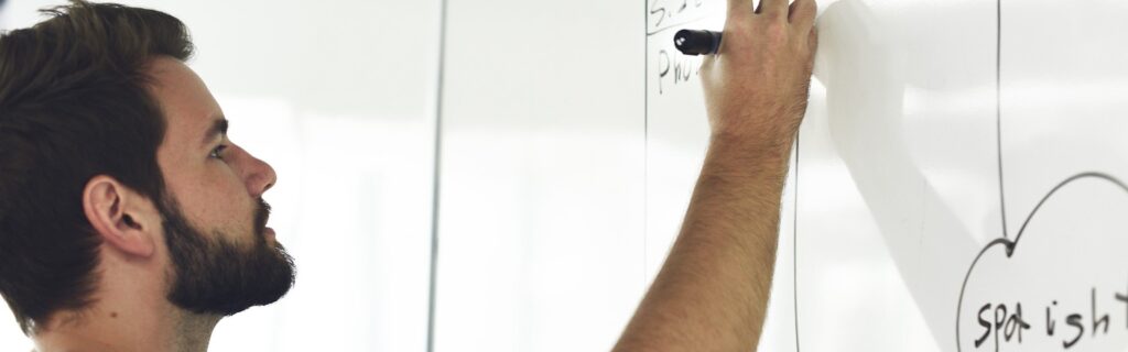 Man schrijft op een whiteboard tijdens een brainstormsessie.