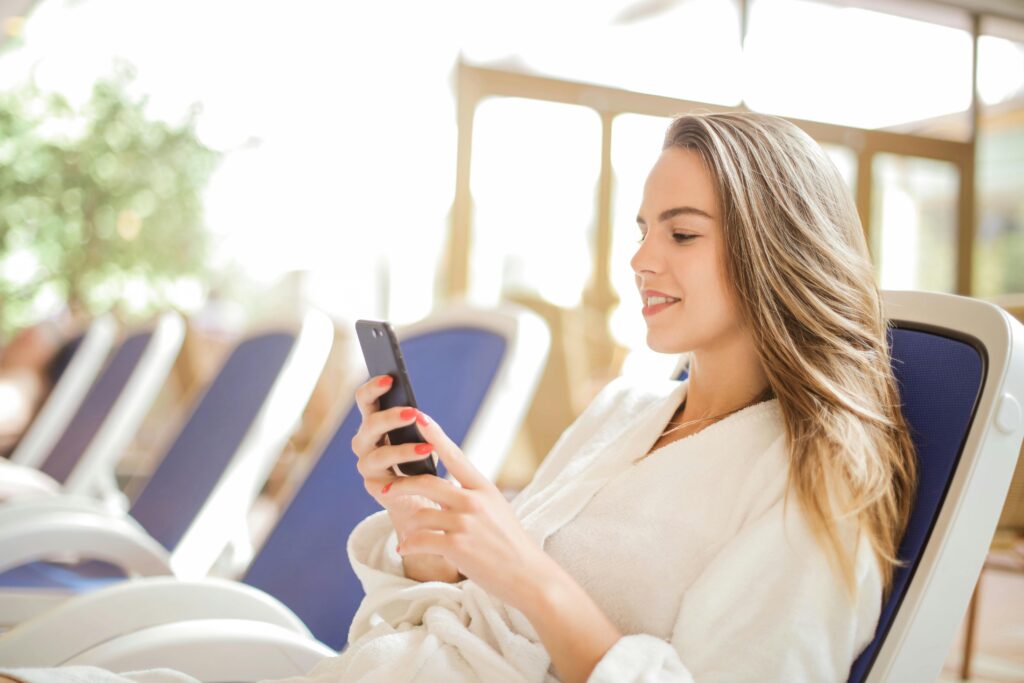 Vrouw zit in een lounge stoel en houdt een telefoon vast terwijl ze ernaar kijkt.