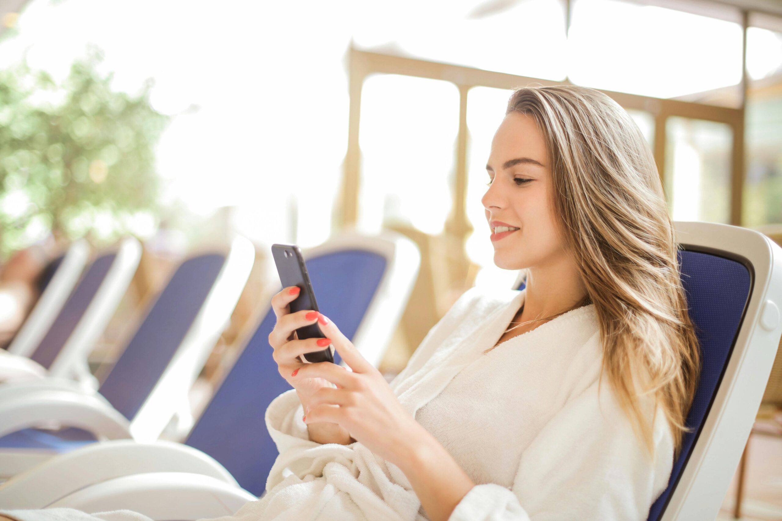 Vrouw zit in een lounge stoel en houdt een telefoon vast terwijl ze ernaar kijkt.