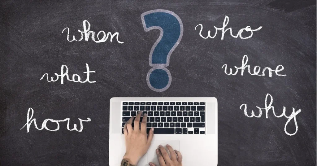 Laptop met vraagwoorden zoals who, what, when, where, why en how op een schoolbord.