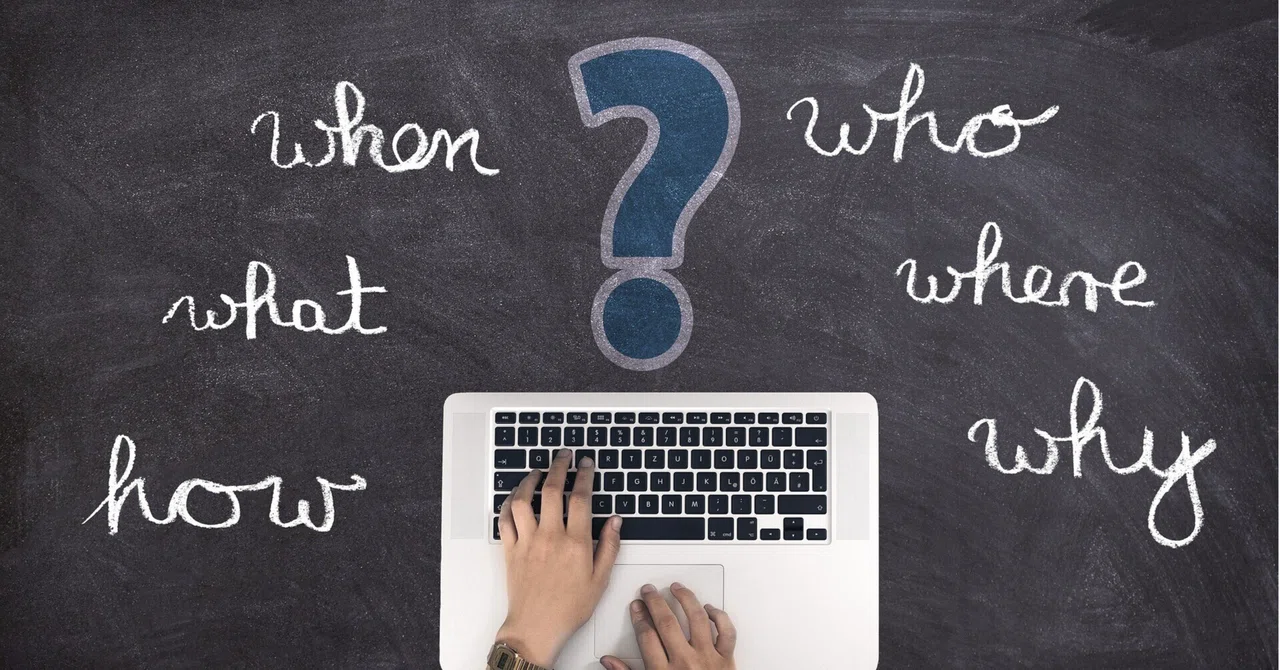 Laptop met vraagwoorden zoals who, what, when, where, why en how op een schoolbord.