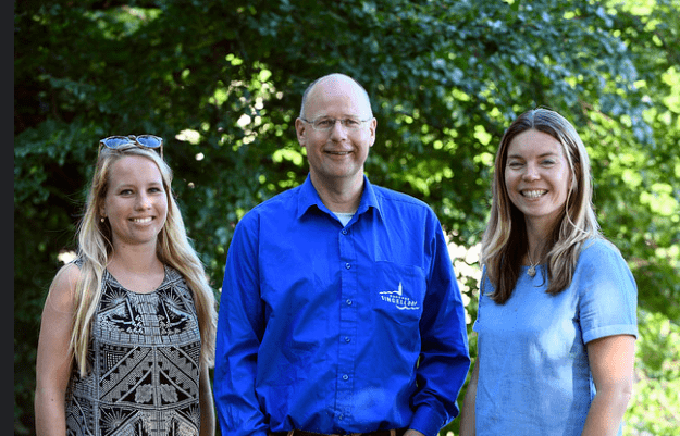 Drie organisatoren van de Singelloop Breda poseren voor een teamfoto buiten.
