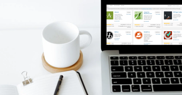 Laptop met WordPress plugin overzicht op het scherm naast een notitieboek en koffiekop op bureau.